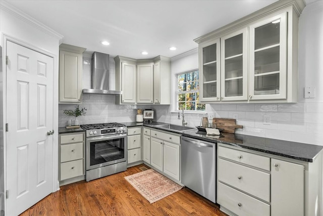 kitchen featuring sink, wall chimney exhaust hood, ornamental molding, appliances with stainless steel finishes, and dark hardwood / wood-style flooring