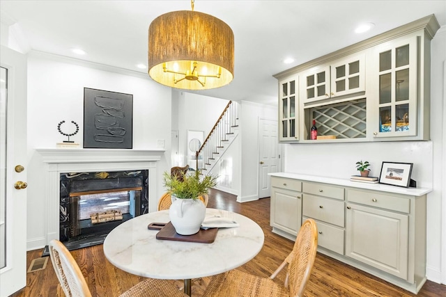 dining space with a fireplace, ornamental molding, a chandelier, and dark wood-type flooring