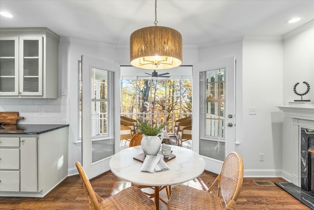 dining space with dark hardwood / wood-style floors, ceiling fan, ornamental molding, and a high end fireplace