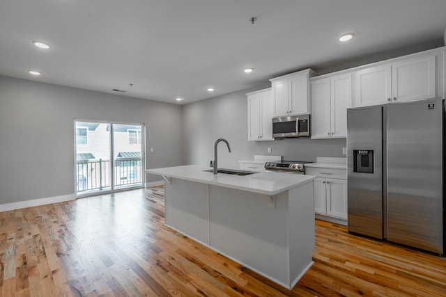 kitchen with a center island with sink, white cabinets, sink, light hardwood / wood-style flooring, and appliances with stainless steel finishes