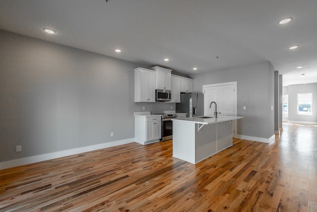 kitchen with appliances with stainless steel finishes, white cabinetry, light hardwood / wood-style flooring, and a kitchen island with sink