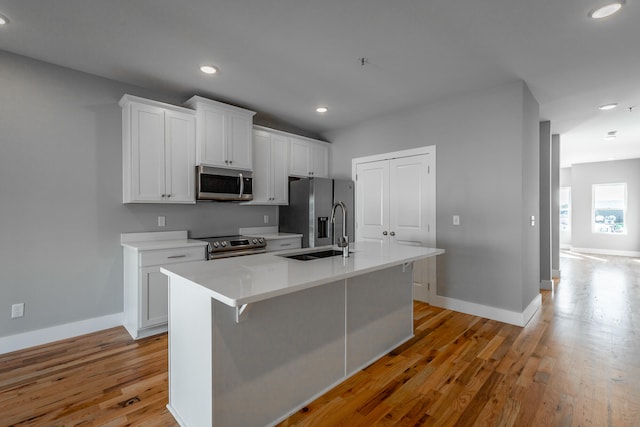 kitchen with white cabinets, stainless steel appliances, a center island with sink, and sink