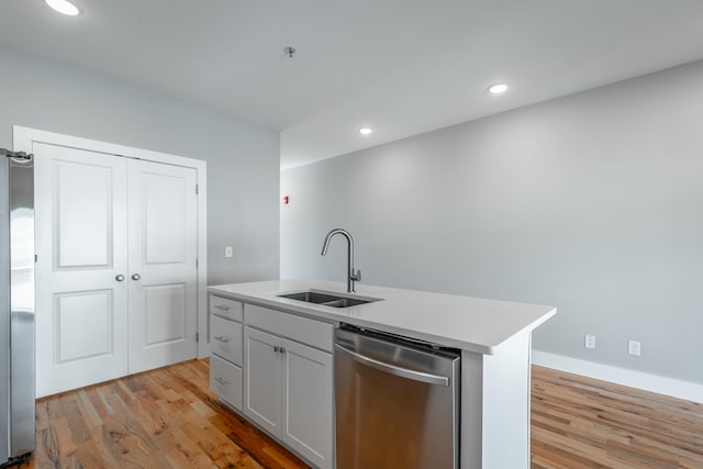 kitchen with dishwasher, sink, light wood-type flooring, and a kitchen island with sink