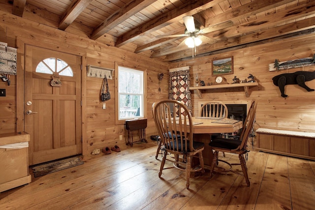 dining space with wood ceiling, light wood-type flooring, wooden walls, beamed ceiling, and ceiling fan