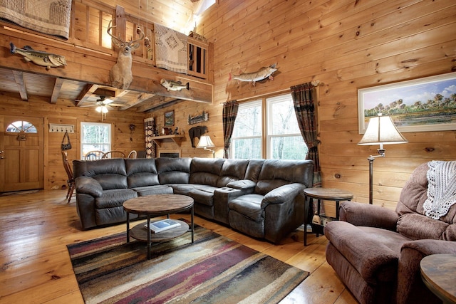 living room featuring beamed ceiling, a healthy amount of sunlight, wooden walls, and light wood-type flooring