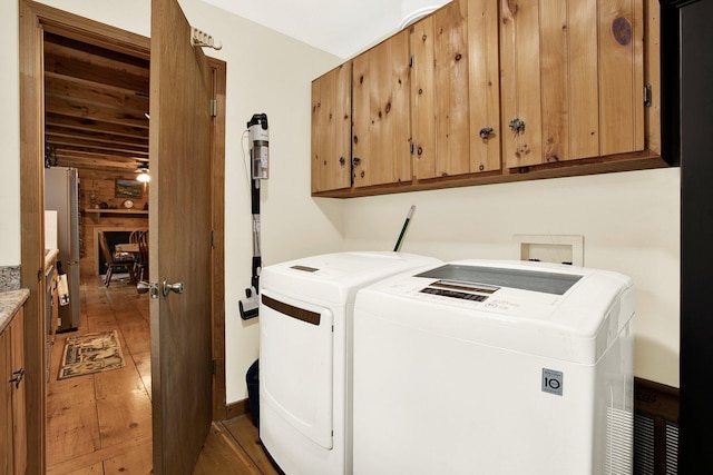 clothes washing area featuring washer and dryer, wood-type flooring, and cabinets