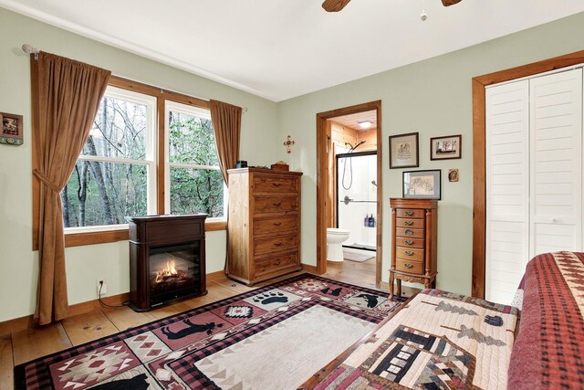 bedroom featuring connected bathroom, light hardwood / wood-style flooring, a closet, and ceiling fan