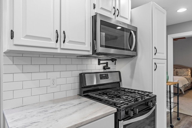 kitchen with decorative backsplash, light stone counters, stainless steel appliances, hardwood / wood-style flooring, and white cabinets