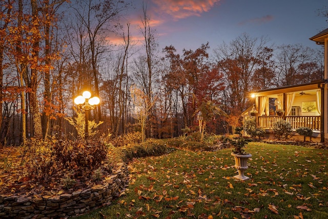 yard at dusk featuring covered porch and ceiling fan