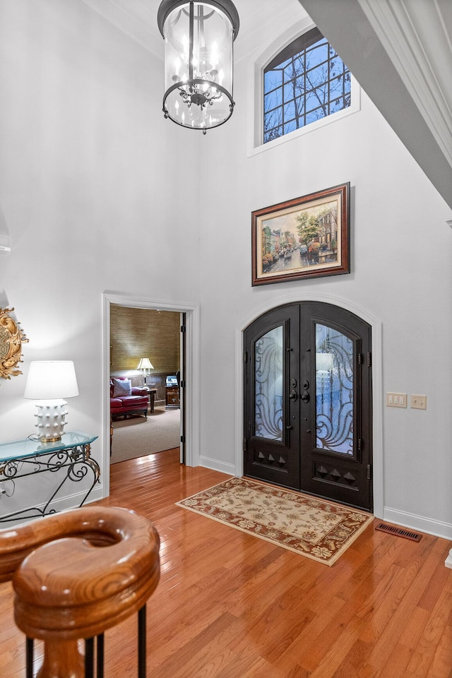 entryway with hardwood / wood-style floors, crown molding, a high ceiling, and french doors