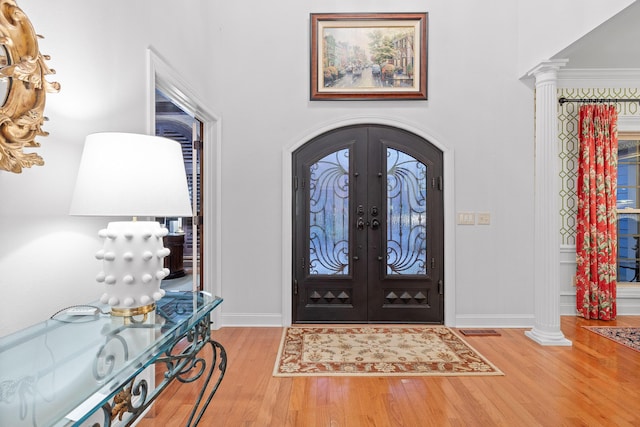 foyer entrance with decorative columns, french doors, and light wood-type flooring