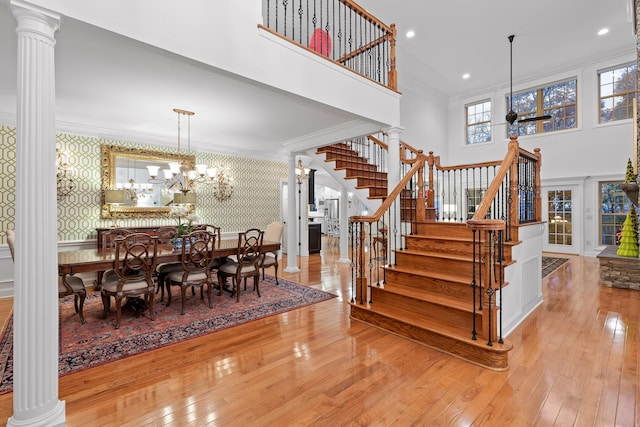 dining area with decorative columns, a high ceiling, light hardwood / wood-style flooring, ornamental molding, and a chandelier