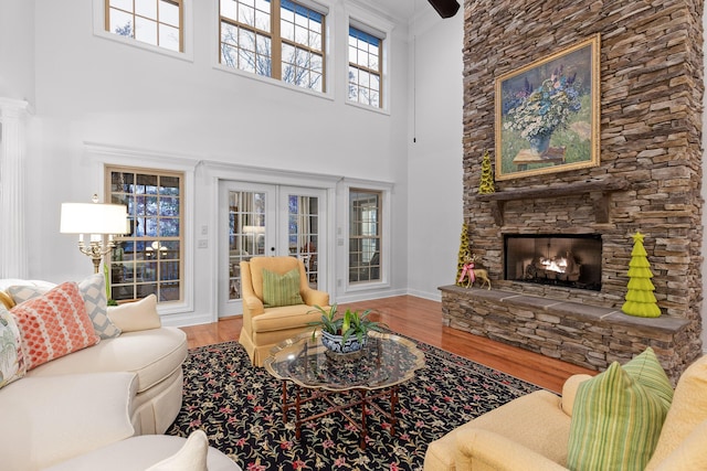 living room featuring a fireplace, wood-type flooring, a towering ceiling, and french doors