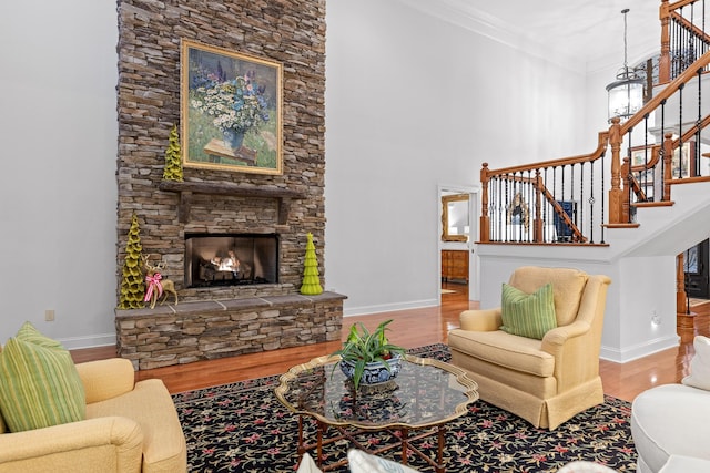 living room with hardwood / wood-style floors, a towering ceiling, a stone fireplace, and crown molding