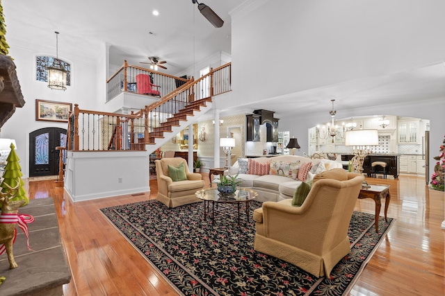 living room featuring french doors, a high ceiling, light hardwood / wood-style floors, ceiling fan with notable chandelier, and ornamental molding