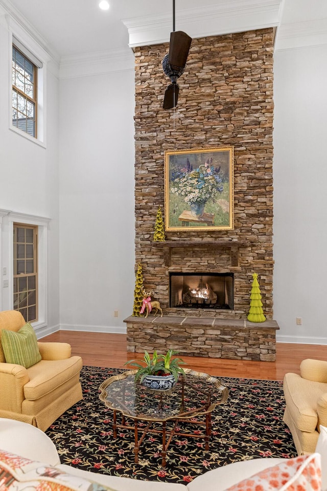 living room with hardwood / wood-style flooring, a stone fireplace, ceiling fan, and crown molding