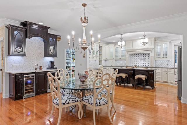 dining space with light wood-type flooring, crown molding, and wine cooler