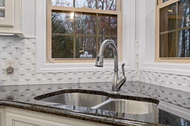 interior details featuring white cabinets, decorative backsplash, sink, and dark stone counters