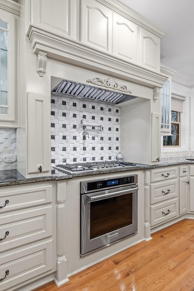 kitchen featuring backsplash, crown molding, light hardwood / wood-style flooring, appliances with stainless steel finishes, and custom range hood