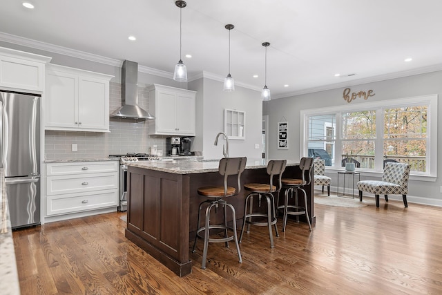 kitchen featuring light stone countertops, white cabinets, wall chimney exhaust hood, stainless steel appliances, and a center island with sink