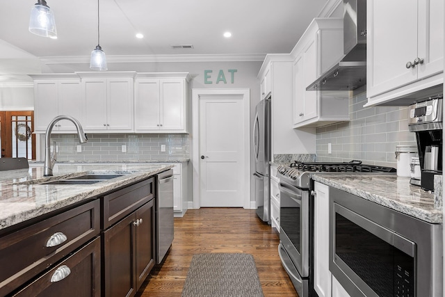 kitchen featuring appliances with stainless steel finishes, pendant lighting, wall chimney exhaust hood, white cabinets, and sink