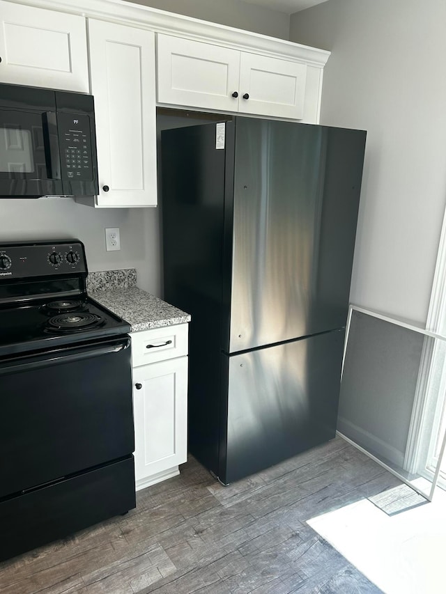 kitchen featuring light stone countertops, light wood-type flooring, white cabinetry, and black appliances