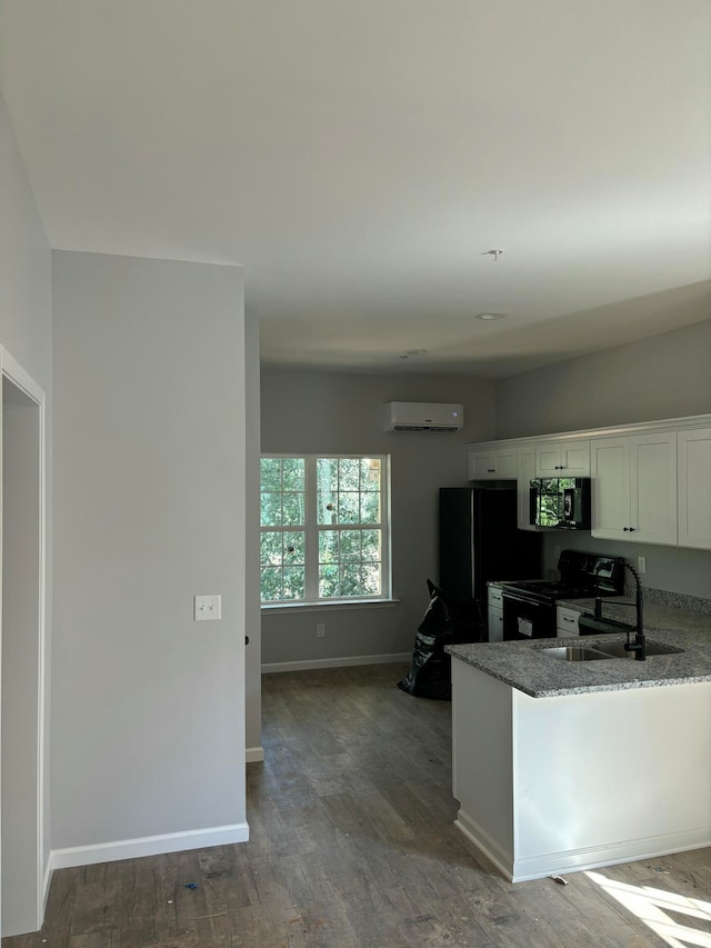 kitchen with white cabinetry, sink, a wall mounted AC, dark stone counters, and black appliances