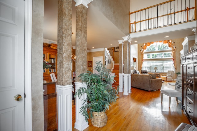 interior space featuring hardwood / wood-style flooring, ornate columns, ornamental molding, and a high ceiling