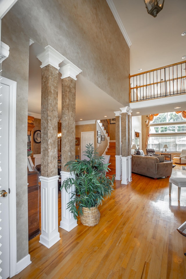 interior space featuring hardwood / wood-style floors, a towering ceiling, crown molding, and decorative columns