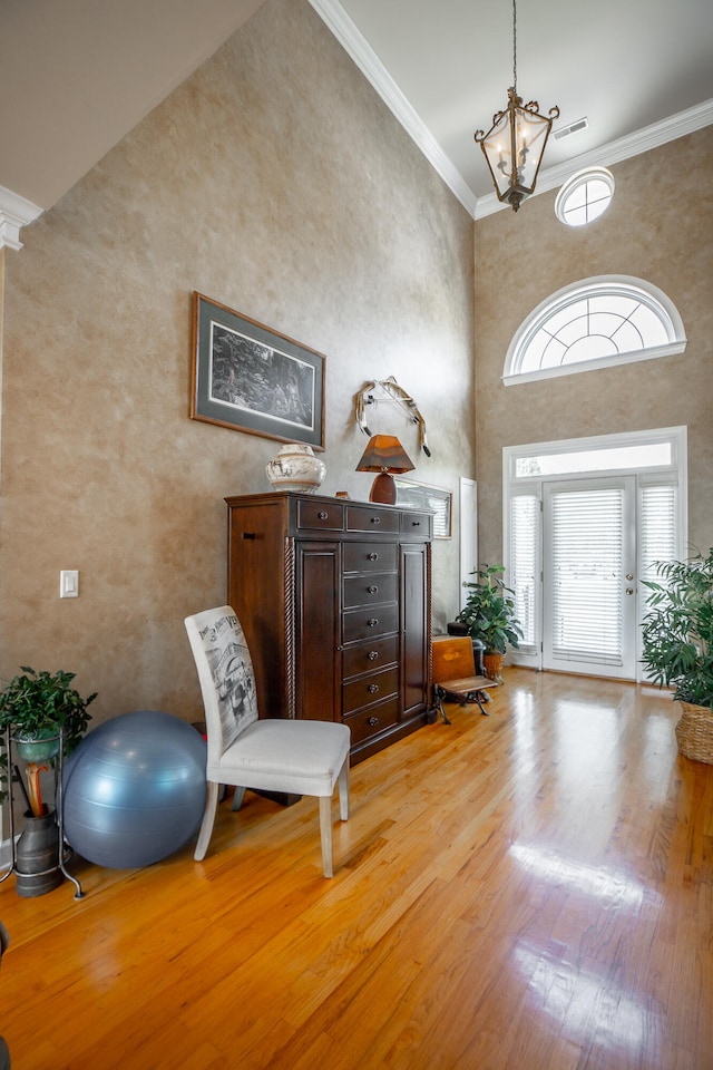 entrance foyer with light hardwood / wood-style floors, ornamental molding, a towering ceiling, and an inviting chandelier