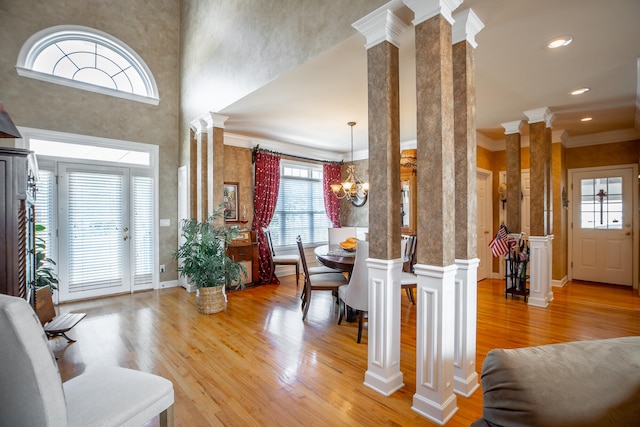 foyer with an inviting chandelier, light hardwood / wood-style flooring, decorative columns, crown molding, and a towering ceiling