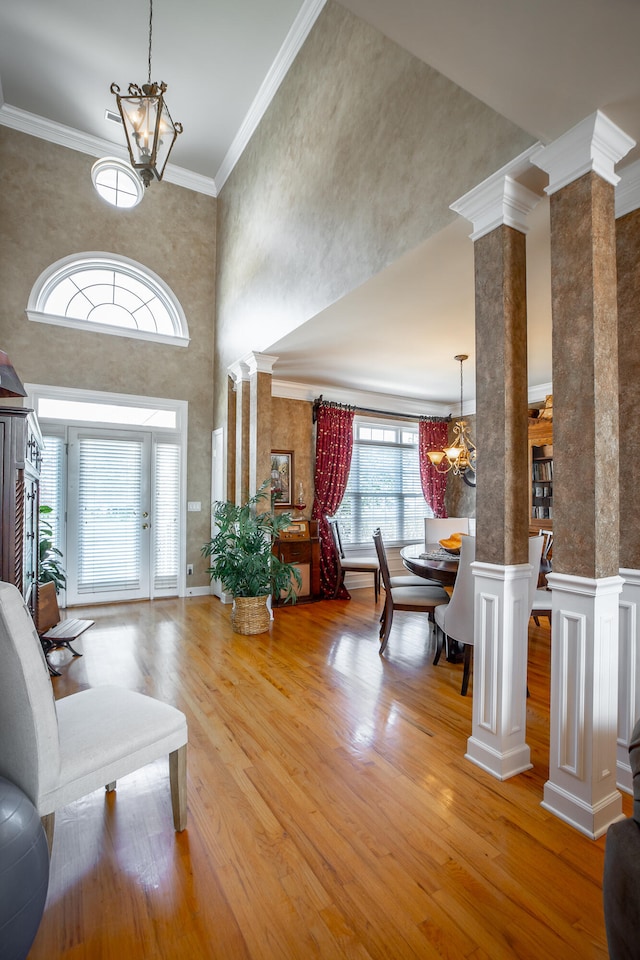 entryway featuring ornate columns, ornamental molding, hardwood / wood-style flooring, a chandelier, and a high ceiling