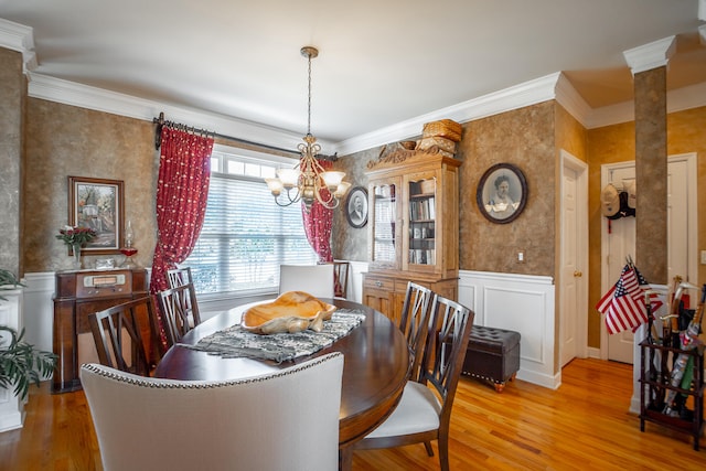 dining area with light hardwood / wood-style floors, decorative columns, ornamental molding, and a notable chandelier