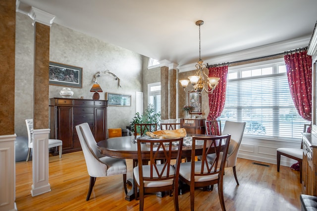 dining area featuring decorative columns, crown molding, an inviting chandelier, and light wood-type flooring