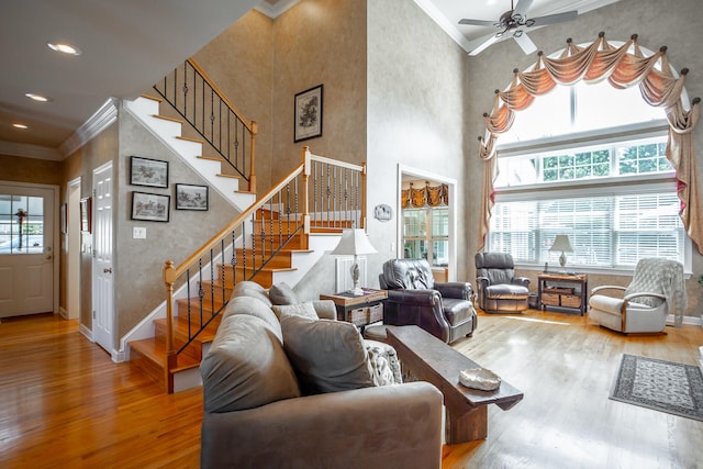 living room with a towering ceiling, hardwood / wood-style flooring, ceiling fan, and ornamental molding