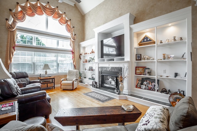 living room with built in features, wood-type flooring, a high end fireplace, and vaulted ceiling