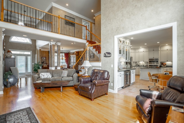 living room featuring wine cooler, light wood-type flooring, ornamental molding, and a high ceiling