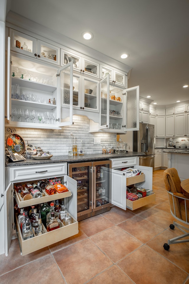 bar featuring decorative backsplash, stainless steel refrigerator with ice dispenser, white cabinetry, wine cooler, and light tile patterned flooring