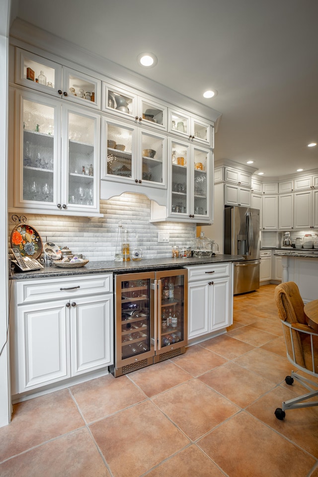 bar with decorative backsplash, stainless steel fridge, beverage cooler, light tile patterned floors, and white cabinets