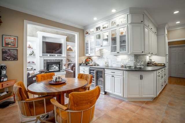 kitchen featuring a high end fireplace, white cabinets, wine cooler, ornamental molding, and tasteful backsplash