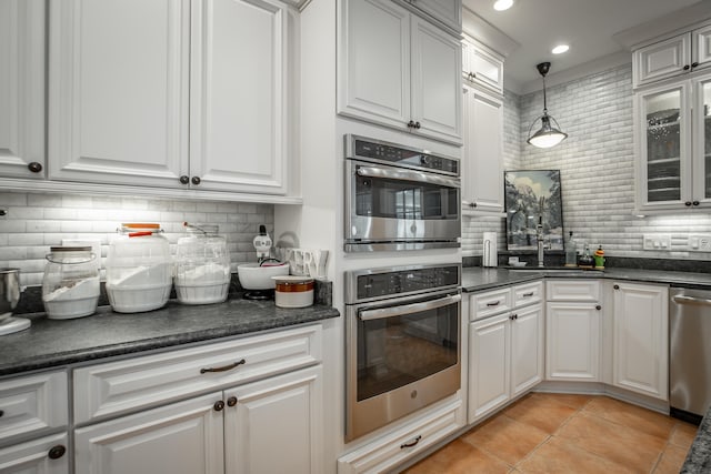 kitchen with decorative backsplash, stainless steel appliances, light tile patterned floors, white cabinetry, and hanging light fixtures