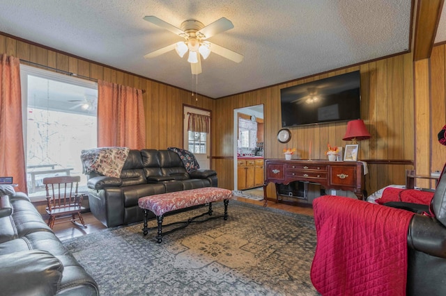 living room featuring a textured ceiling, ceiling fan, crown molding, and wood walls