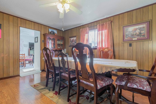 dining space with light hardwood / wood-style floors, ceiling fan, and wooden walls