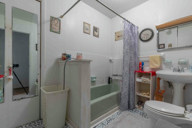 bathroom with tile walls, shower / bath combo with shower curtain, a textured ceiling, and toilet