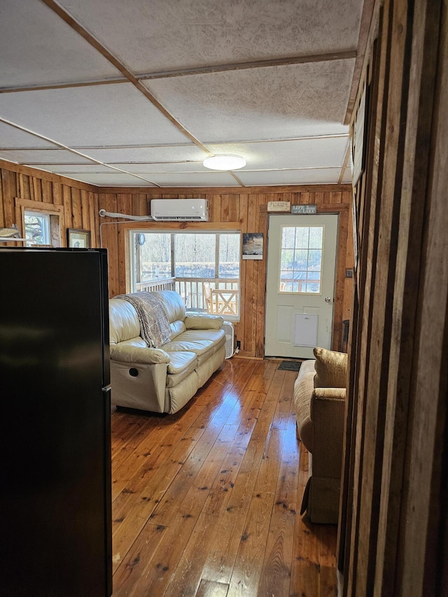 living area with a wealth of natural light, wooden walls, hardwood / wood-style floors, and a wall mounted air conditioner