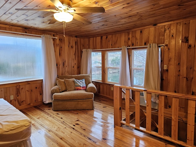 sitting room with wooden ceiling, wood walls, light wood-style flooring, and ceiling fan