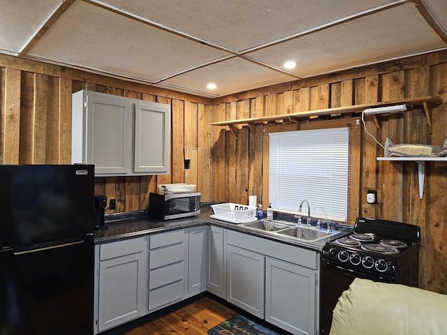 kitchen with wooden walls, dark wood finished floors, dark countertops, black appliances, and a sink