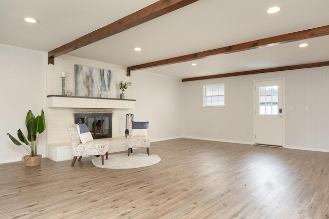 living area with beamed ceiling, ornamental molding, a brick fireplace, and light hardwood / wood-style flooring