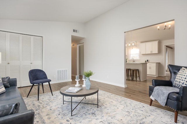 living room featuring light wood-type flooring, lofted ceiling, and a notable chandelier