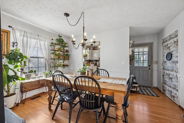 dining room featuring a textured ceiling, light hardwood / wood-style floors, and an inviting chandelier